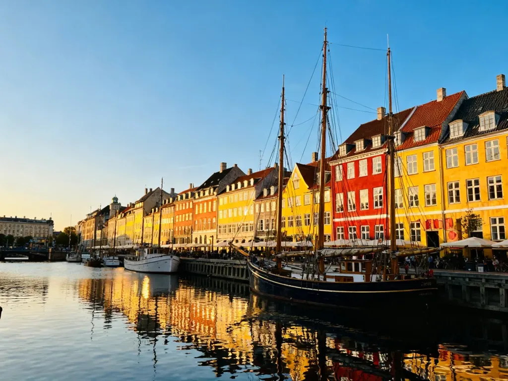 Kolorowe kamienice i zabytkowe żaglowce w porcie Nyhavn w Kopenhadze o zachodzie słońca.