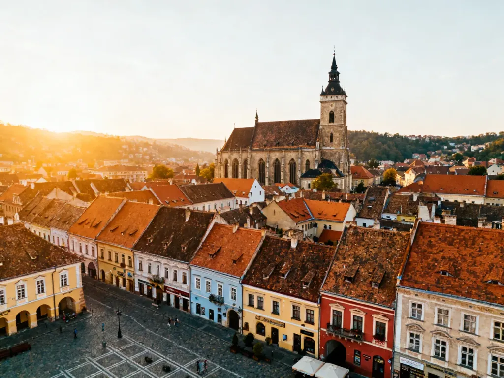 Panoramiczny widok na Rynek w Braszowie z zabytkowym Czarnym Kościołem i kolorowymi kamienicami w świetle zachodzącego słońca.