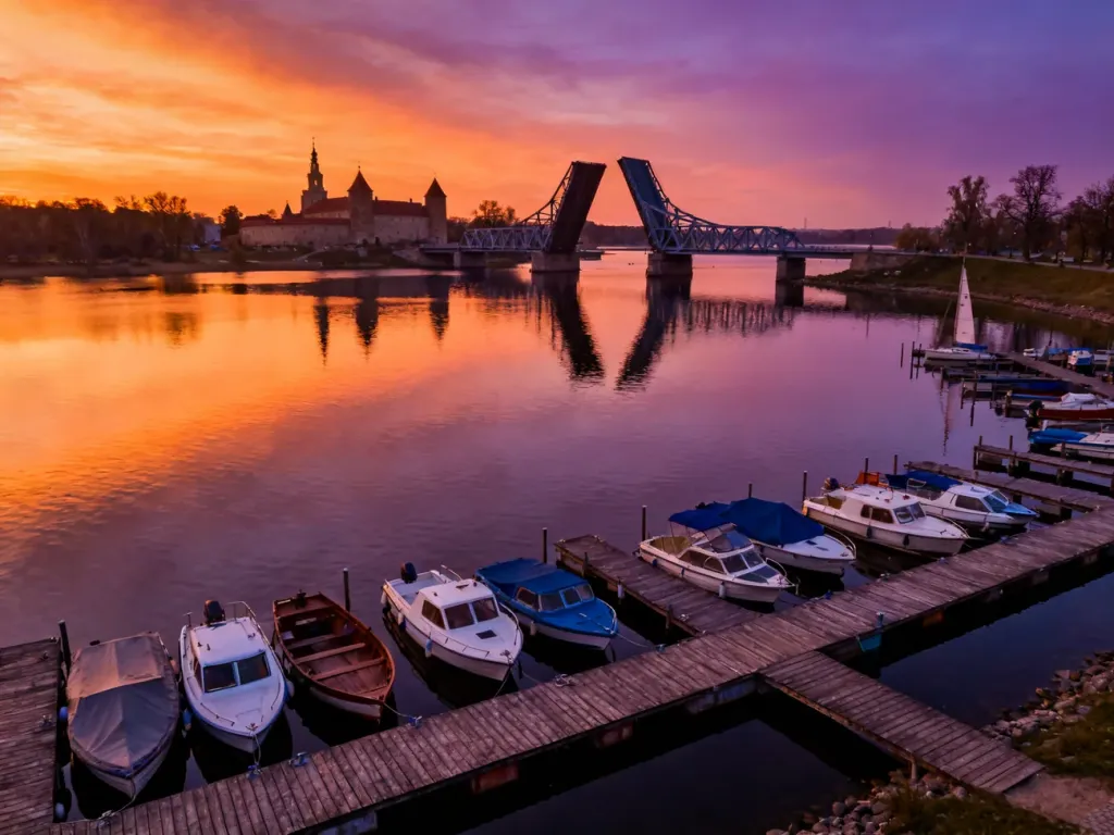 Malownicza marina w Giżycku o zachodzie słońca z widocznym mostem obrotowym i Twierdzą Boyen w tle.
