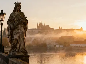 Wąska uliczka w Ostuni z białymi domami i kwitnącą bugenwillą, w tle widoczna kopuła katedry na tle błękitnego nieba.