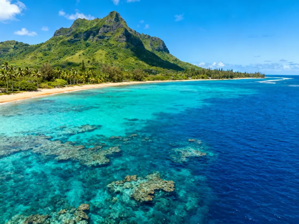 Widok z lotu ptaka na turkusowe wody, rafy koralowe i zielone góry wybrzeża Mauritiusa.