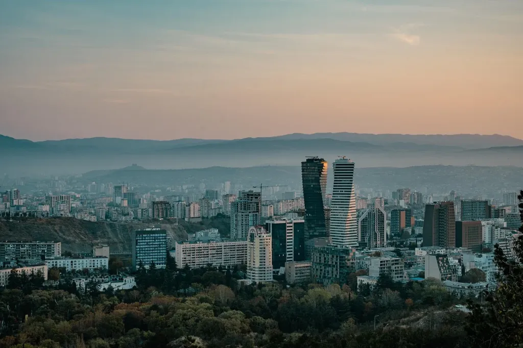 Widok na centrum Tbilisi z nowoczesnym wieżowcem górującym nad tradycyjną zabudową miasta.
